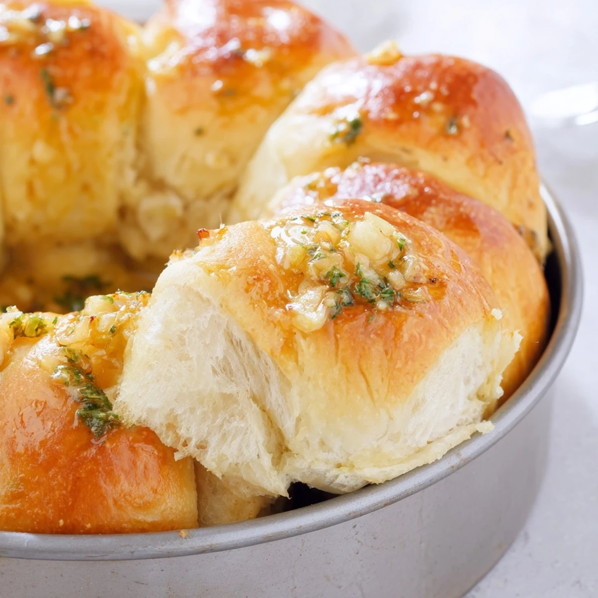 Golden-brown Garlic Butter Bread Pull-Apart rolls glisten with melted butter and flecks of fresh parsley in a round baking pan.