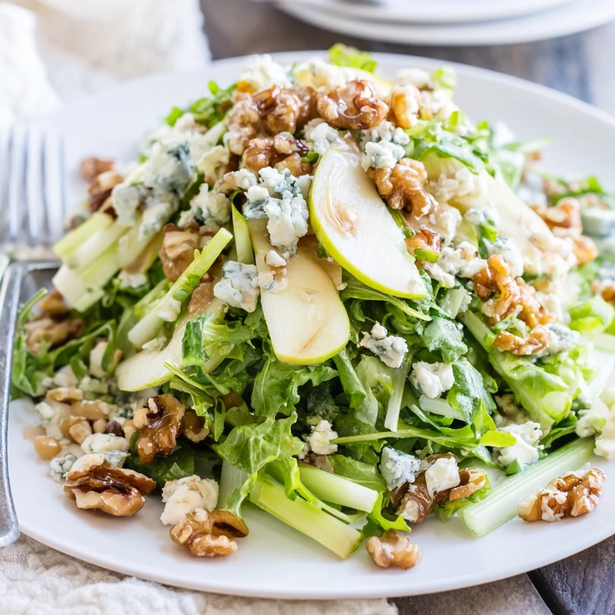 A vibrant bowl of Apple and Walnut Salad topped with crumbled blue cheese, ready to serve alongside roasted chicken or pork for a light winter meal.  