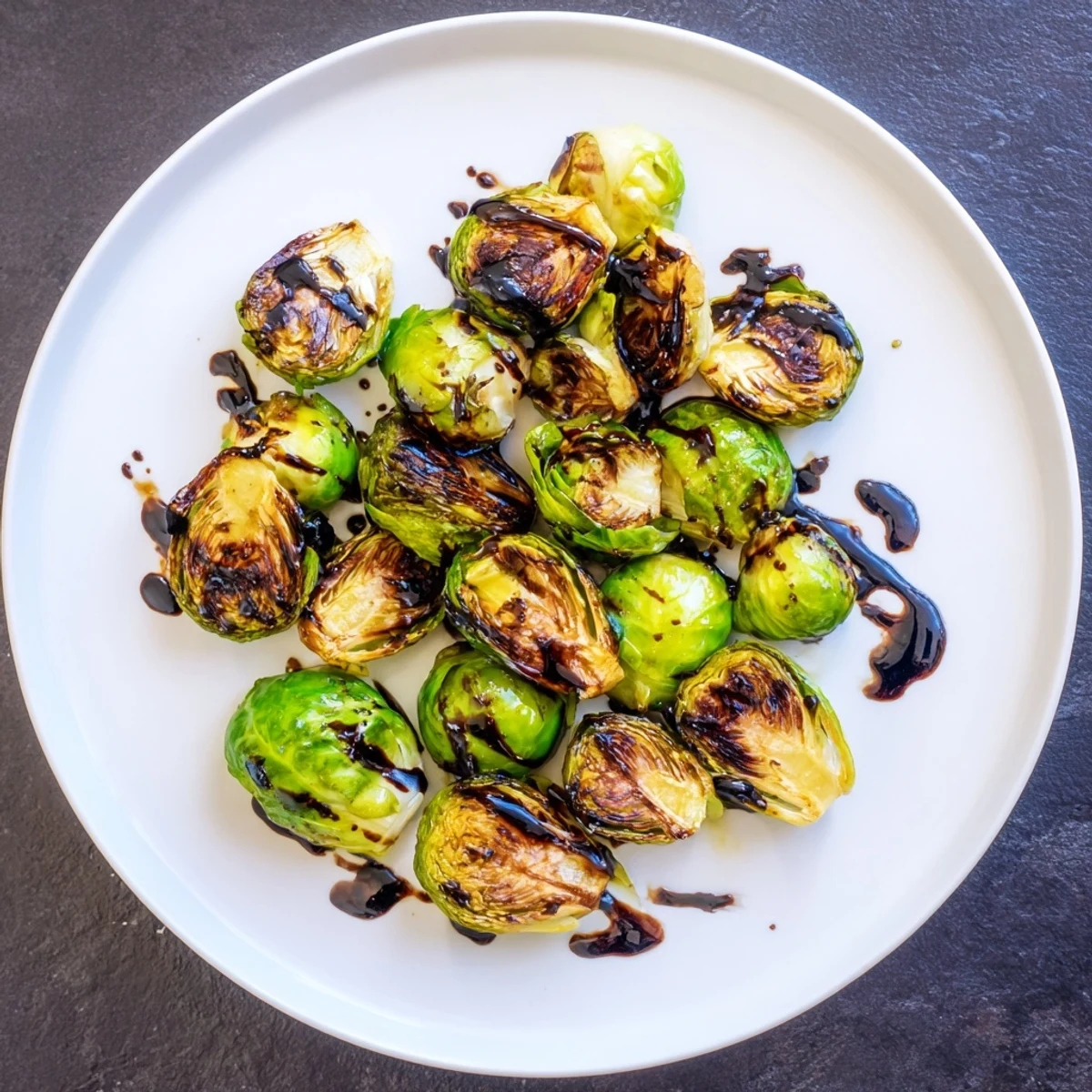 Golden brown roasted Brussels sprouts glistening with balsamic reduction on a white serving platter.  