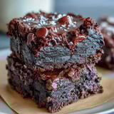 A single slice of Greek Yogurt Brownies is plated with a dollop of whipped cream and fresh raspberries.