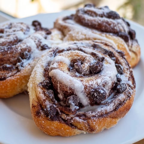 Golden-brown Nutella Chocolate Chip Rolls, fresh from the oven, dripping with glaze and melty chocolate chips on a rustic pan.