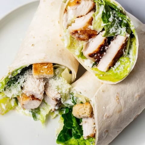 A vibrant Caesar Chicken Salad Wrap, cut in half to reveal layers of juicy grilled chicken, creamy Caesar dressing, and crunchy romaine inside a golden flour tortilla.