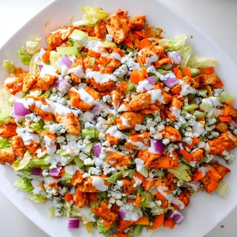 A close-up of a freshly tossed Buffalo Chicken Chopped Salad, showcasing juicy red tomatoes, shredded carrots, and a generous drizzle of ranch dressing.