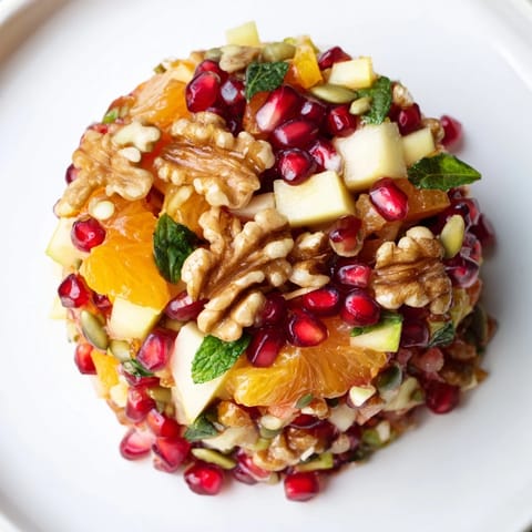 The Pomegranate and Walnut Salad showcases juicy pomegranate arils, orange segments, and fresh mint, drizzled with a honey-lemon dressing for a refreshing bite.