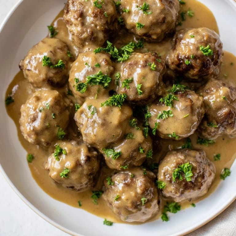 A close-up of a skillet filled with flavorful Swedish Meatballs, freshly cooked and simmering in a brown gravy.