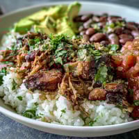 Golden-brown shredded carnitas pile high over fluffy white rice in this hearty bowl, topped with pinto beans and vibrant fresh salsa.