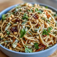 A colorful Asian sesame noodle salad with crunchy vegetables and a creamy peanut dressing, served in a white bowl.  