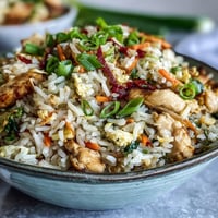 Steamed, vibrant Egg Roll Fried Rice with Chicken fills a white bowl, garnished with fresh green onions for a crispy finish.