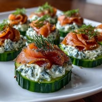 Smoked salmon cucumber bites with creamy herbed cheese and fresh dill on crisp cucumber slices.